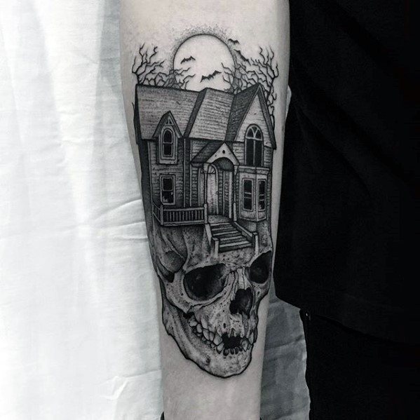 Forearm tattoo of a haunted house resting on a skull, with leafless trees, full moon, and bats flying in the background.