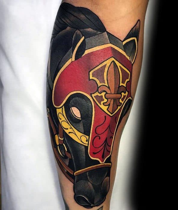 Bold horse head tattoo with red and gold medieval armor design on the upper arm, featuring sharp lines and vibrant shading