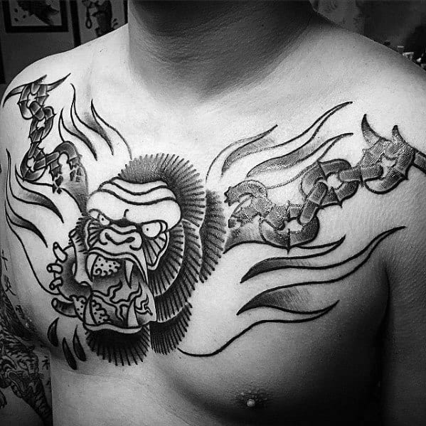 Bold blackwork King Kong chest tattoo with flames and cracked stone design, showing an angry Kong breaking through chains.