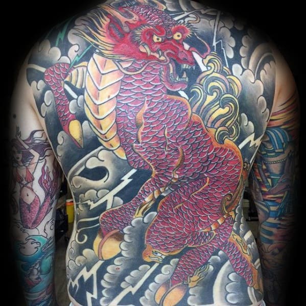 Full-back Kirin tattoo in vibrant red with gold accents, surrounded by storm clouds, lightning, and dynamic traditional patterns.