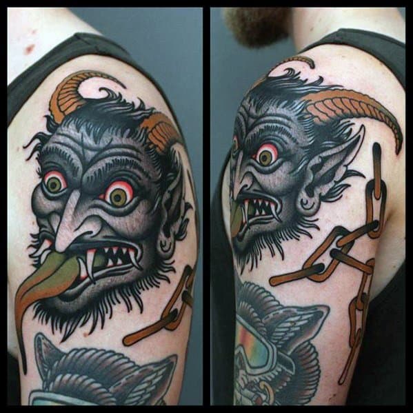 Colorful Krampus tattoo on upper arm showing a horned demon head with a green tongue and broken chains wrapping around the arm.
