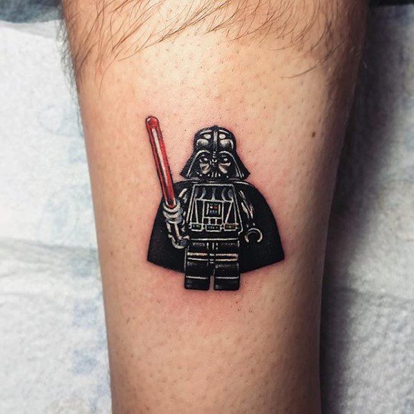 Lego Darth Vader tattoo on leg, featuring detailed black armor, red lightsaber, and cape with realistic shadowing.
