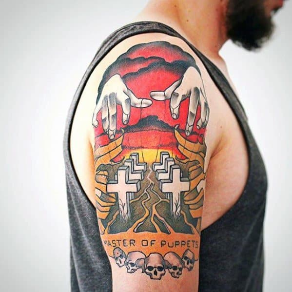 Colorful upper arm tattoo of Metallica’s Master of Puppets album cover with puppet hands, white crosses, and skulls beneath the title.