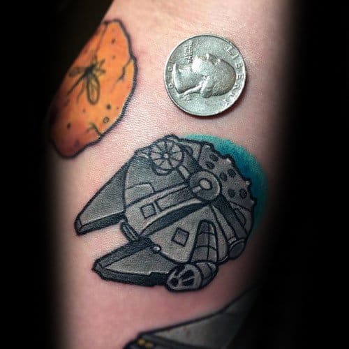 Small Millennium Falcon tattoo with bold black outlines and a blue background, shown next to a coin for size reference.