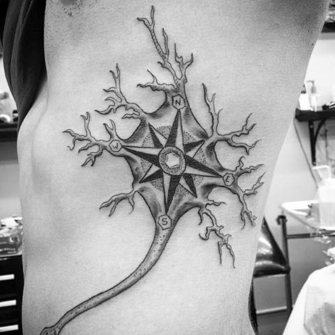 Black and grey neuron tattoo on ribs featuring a compass rose as the cell body, with branching dendrites and detailed shading.