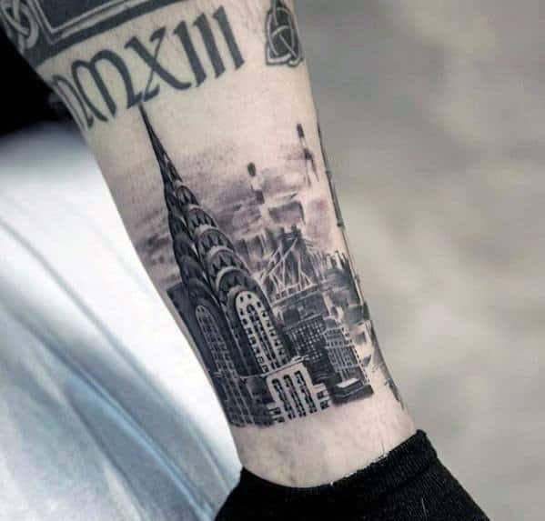 Detailed black and gray forearm tattoo of the Chrysler Building with a misty New York City skyline and bridge in the background.