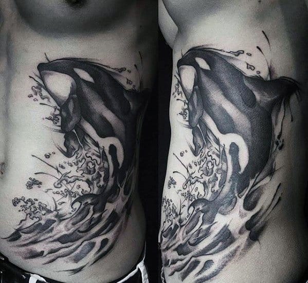Black and gray tattoo on the side and upper arm, featuring an orca whale leaping out of the water with dynamic splashes, creating a sense of movement and power.