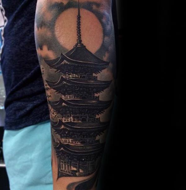 Dark Japanese pagoda tattoo with a full moon backdrop, detailed shading and clouds wrapping around the forearm.