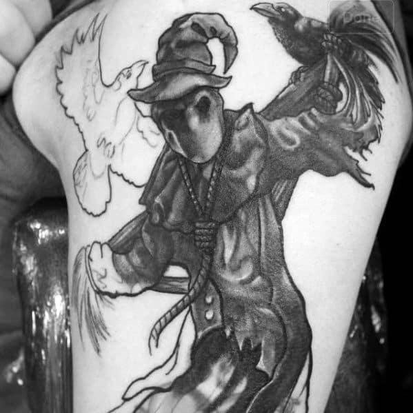 Dark scarecrow tattoo with a faceless hood, tattered cloak, perched crow, and flying dove, shaded in bold black and grey.