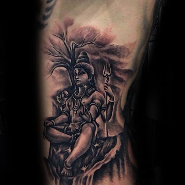 Tattoo of Lord Shiva meditating beneath a tree, holding a trident, with soft shading and a mystical aura surrounding the serene forest scene.