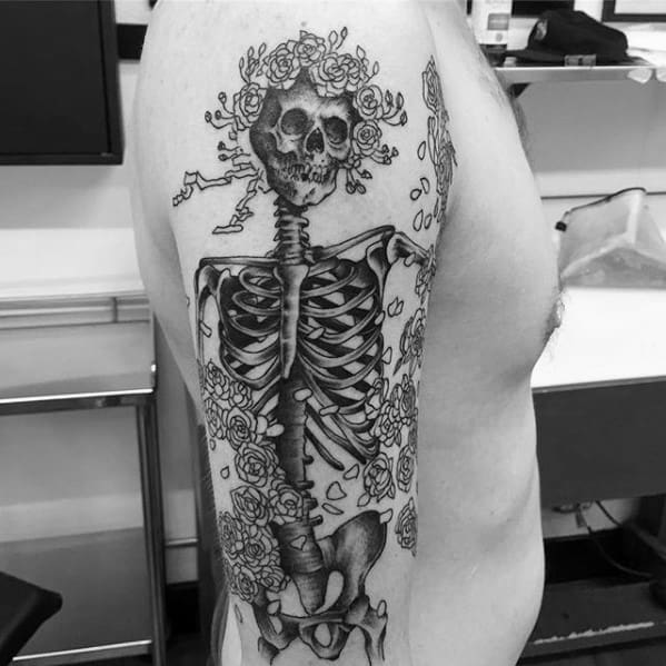 Large Grateful Dead skeleton tattoo with floral crown and roses wrapping around the body, done in detailed black and grey.