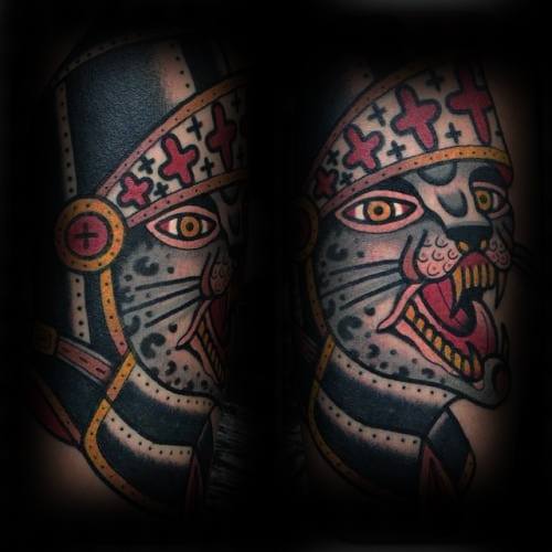 Snow leopard tattoo featuring a medieval knight helmet and cross-covered crown, blending feline fierceness with warrior symbolism.