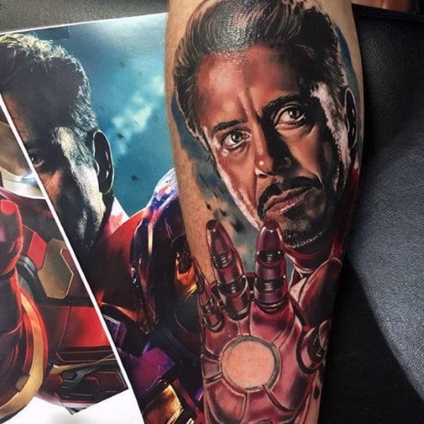 Iron Man tattoo featuring a realistic portrait of Tony Stark with his iconic hand raised, showing the detailed arc reactor and armor elements, blending realism and superhero imagery.