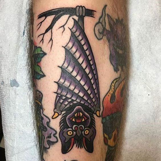 Colorful traditional tattoo of a bat hanging upside down from a branch, featuring bold outlines and vibrant purple tones.