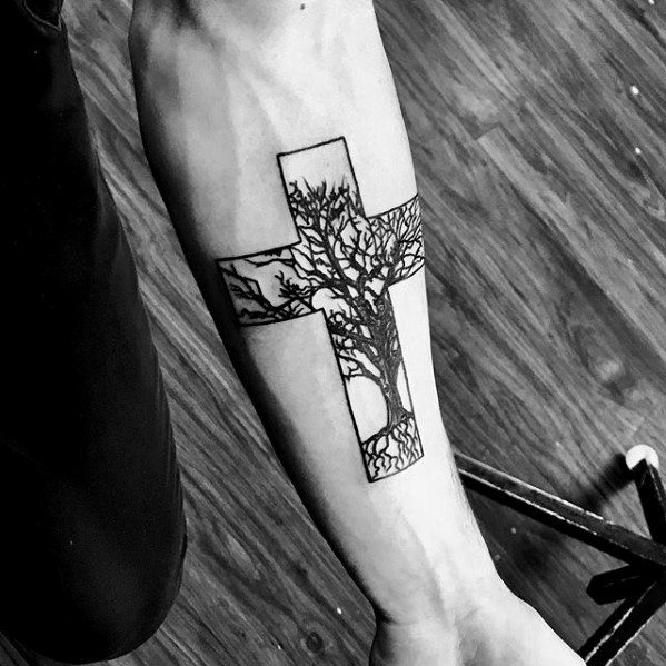Minimalist cross tattoo with a detailed leafless tree design inside, symbolizing life and growth, placed on the inner forearm.
