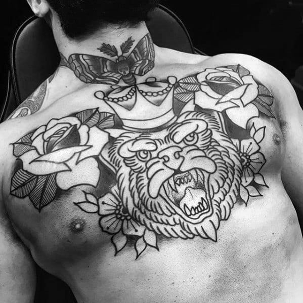 Large black and grey tattoo of a roaring crowned lion with roses, covering the chest and upper shoulders in bold traditional style.