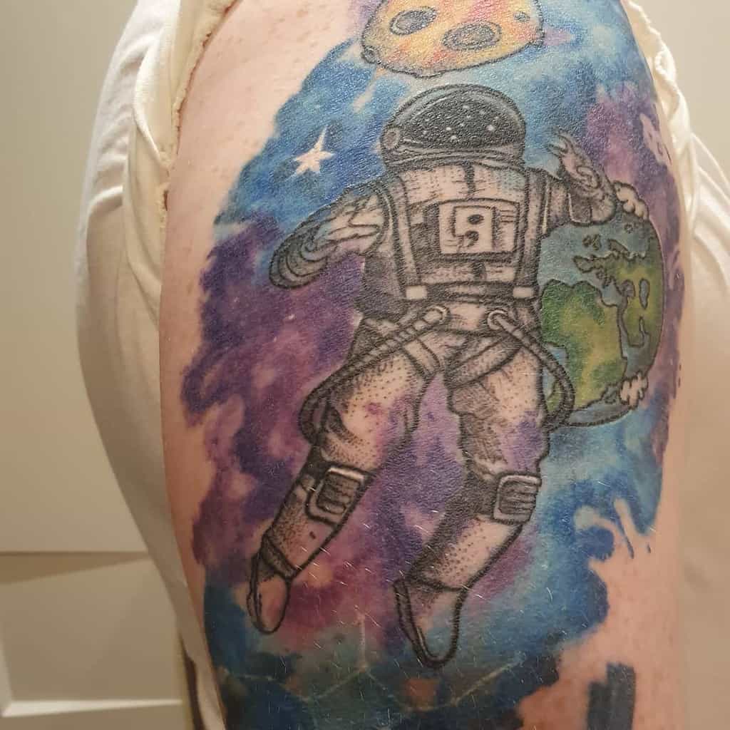 This tattoo depicts an astronaut floating in space, with the number 9 prominently displayed on the astronaut's suit and a vivid background. The artwork includes the Earth, cosmic elements, and bright colors, conveying a sense of exploration and vastness.