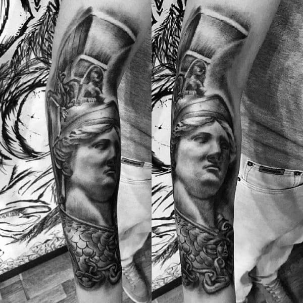 Realistic Athena tattoo sleeve featuring a sculpted face, helmet detail, and textured armor with deep black and grey shading