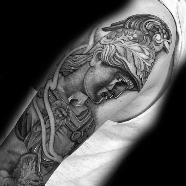 Athena tattoo on upper arm with downward gaze, ornate helmet, and detailed armor in a sculptural black and grey realism style