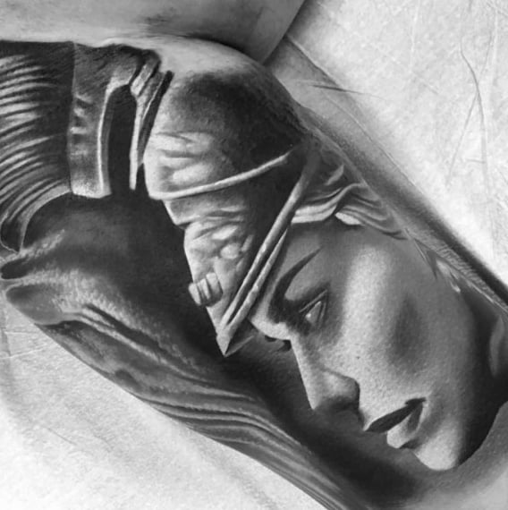Realistic Athena tattoo in profile with soft facial shading, crested helmet, and detailed highlights on the upper arm