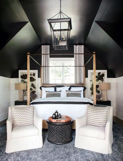 Two-tone black and white bedroom with four-poster bed candelabra chandelier and seating area.