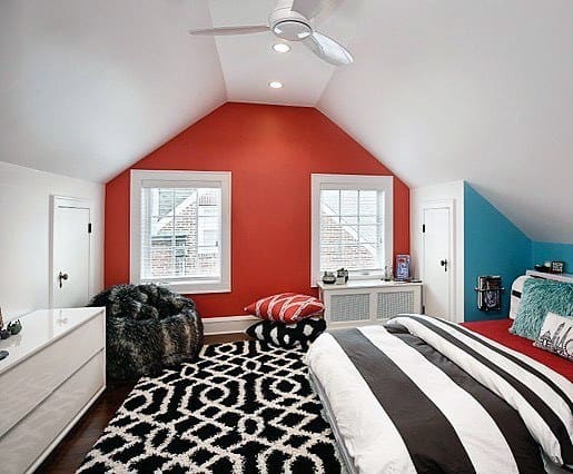 Attic bedroom with sloped ceiling, red accent wall, striped bedding, patterned rug, and cozy bean bag chairs