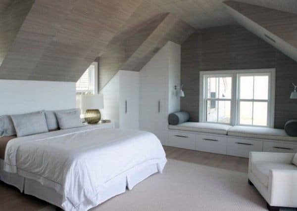 Attic bedroom with white bed, window seat, and built-in storage.