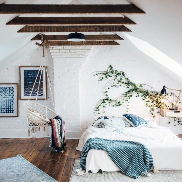 Cozy attic bedroom with wooden beams, a hanging chair, white bed, and ivy on a white brick wall