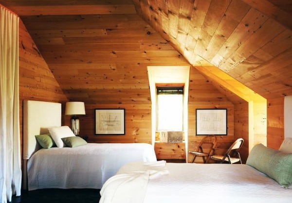 Cozy wood-paneled attic bedroom with two beds, a window, framed art, and a small lamp