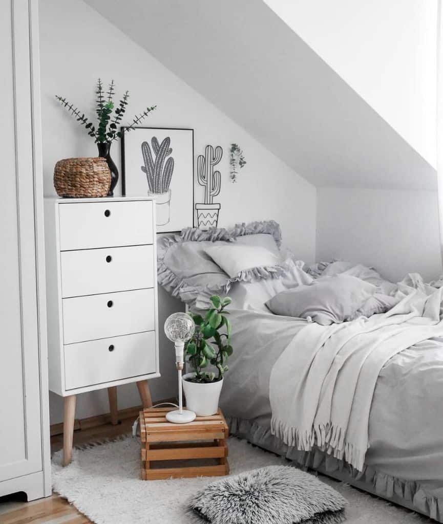 Cozy attic bedroom with a white dresser, plants, and cactus artwork, featuring soft gray bedding and rugs