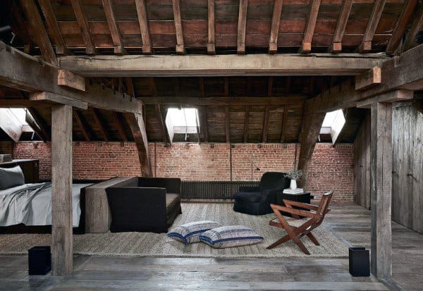 Rustic attic retreat with exposed beams, brick walls, cozy seating, and plush pillows on a wooden floor