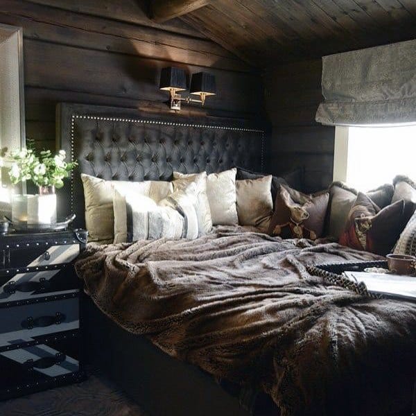 Cozy attic bedroom with tufted headboard, plush pillows, fur blanket, window shades, and a bouquet on the nightstand
