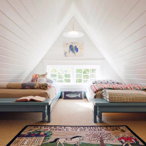 Cozy attic bedroom with two beds, colorful quilts, a pendant light, and a window showcasing lush greenery
