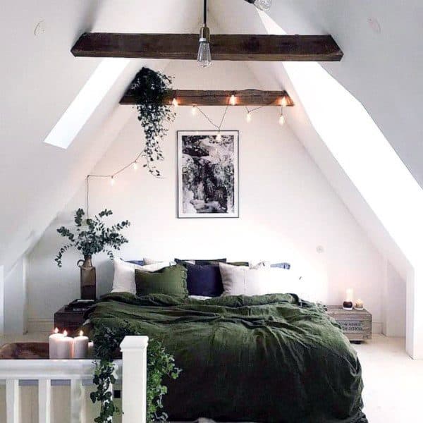 Charming attic bedroom with a green bedspread, plants, candles, and twinkling string lights under wooden beams
