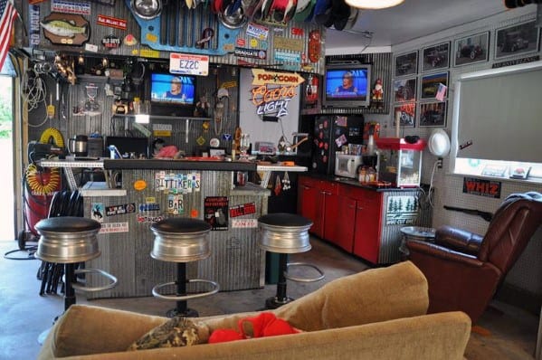 A garage bar with metal stools, a popcorn machine, and car memorabilia on the walls, creating a cozy, vintage atmosphere