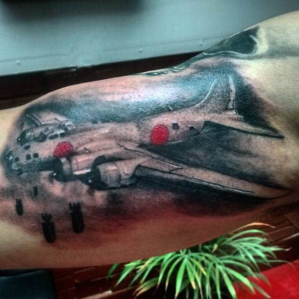 Tattoo of a WW2 bomber airplane dropping bombs on a person's inner arm above the elbow