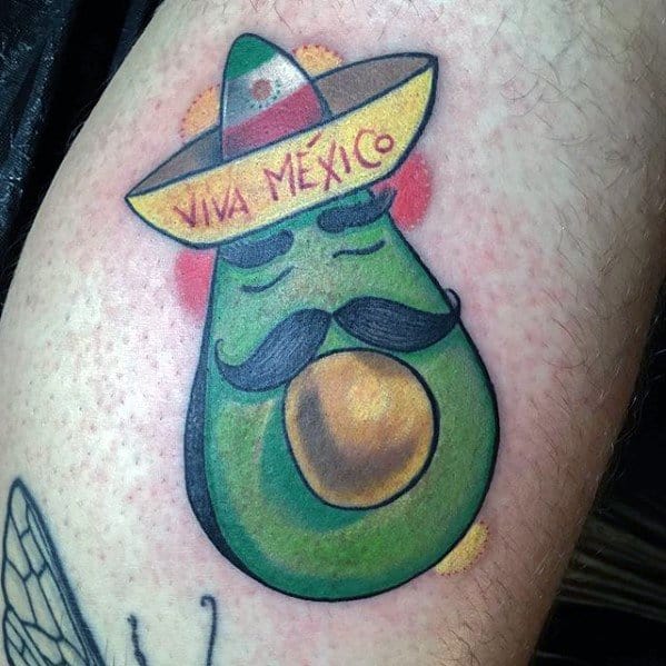 Playful avocado tattoo with a mustache, sombrero, and “Viva Mexico” text, featuring bright colors and a cartoon style.