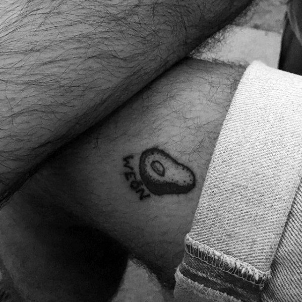 Minimalist avocado tattoo with the word “WEEN” below it, done in simple black ink on the ankle.