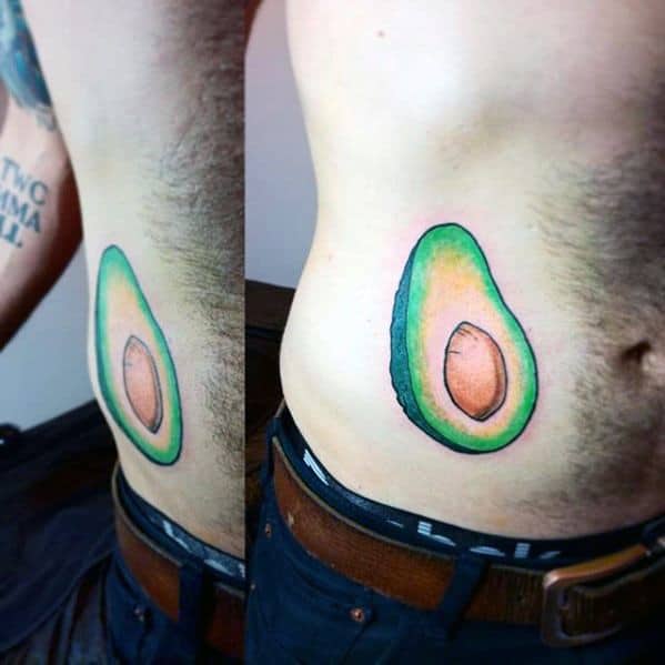 Bright and bold avocado tattoo on the side torso, featuring clean lines and vibrant green and brown shading.