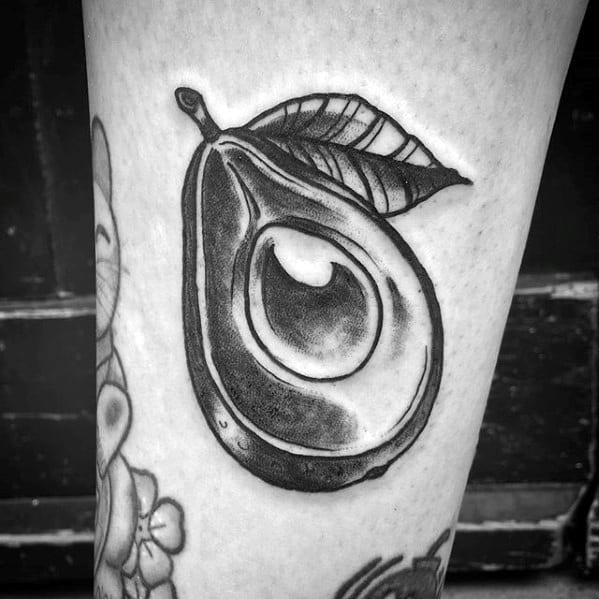 Black and grey avocado tattoo with a bold outline and leaf detail, featuring high contrast shading for a dramatic look.