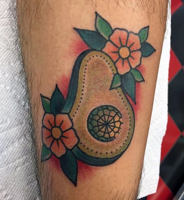 Traditional-style avocado tattoo with bold outlines, decorative pit, and floral accents, featuring vibrant colors and classic shading.