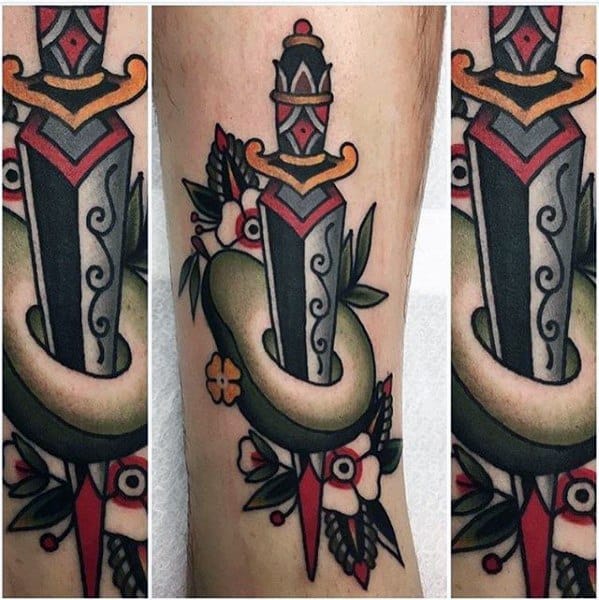 Traditional-style avocado tattoo pierced by a dagger, surrounded by bold flowers and leaves, done in striking red, green, and black tones.