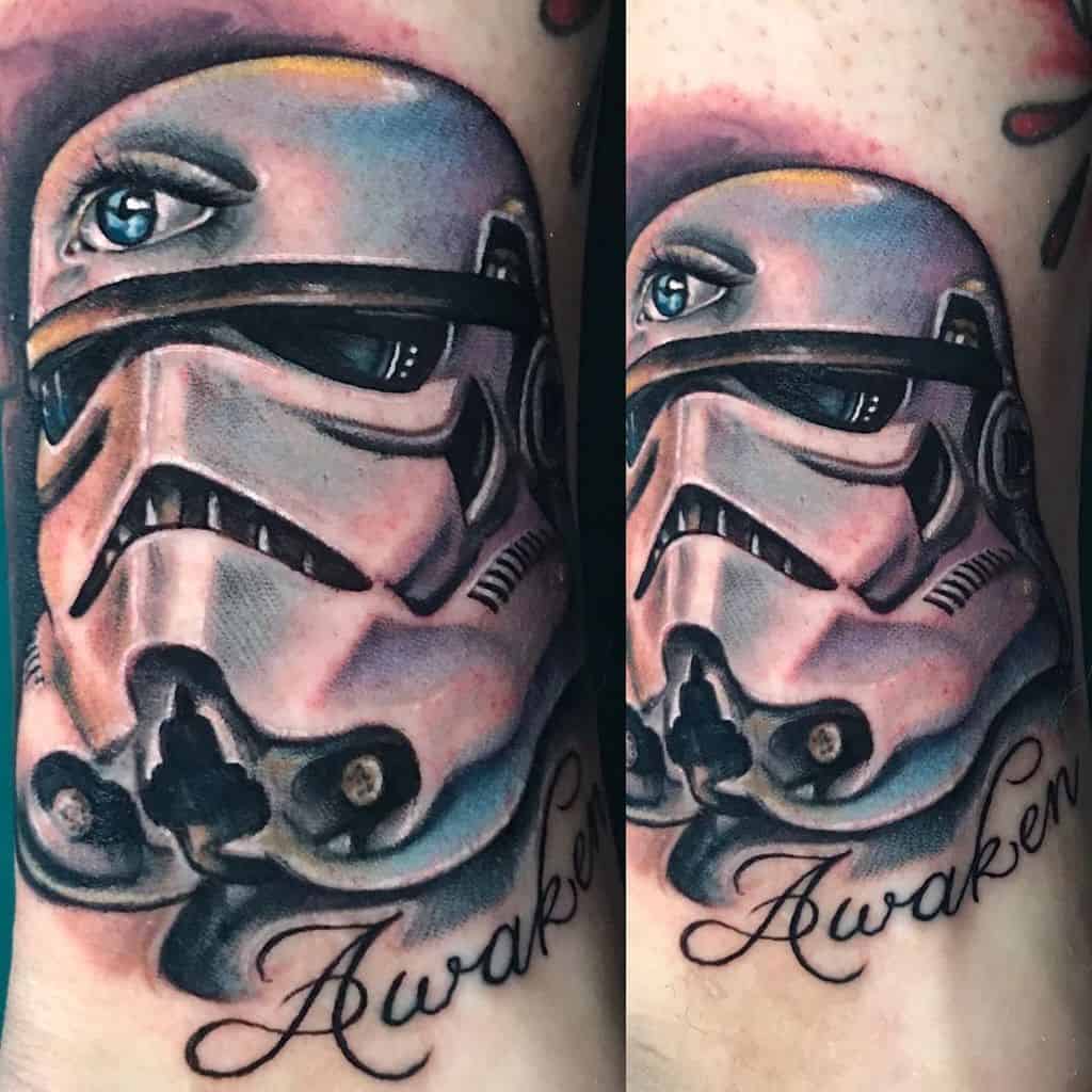 Tattoo of a Stormtrooper helmet with a realistic human eye inside, featuring shading and color details, with 'Awaken' written below.