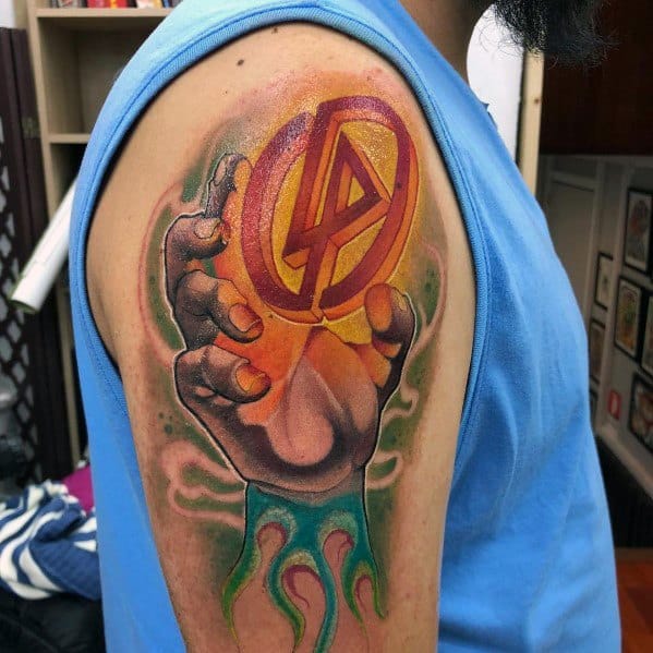 Colorful Linkin Park tattoo featuring a hand gripping the LP logo, surrounded by fiery and smoky effects on the upper arm.