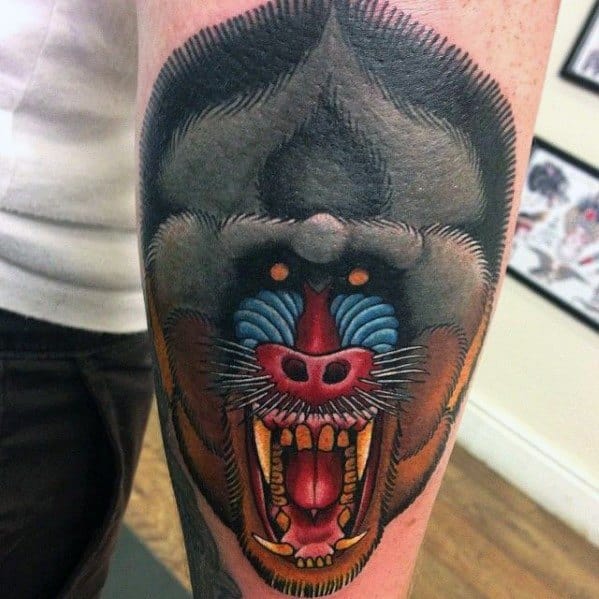 Bold baboon tattoo with fierce expression, vivid blue and red facial details, and sharp teeth, creating a powerful and intense forearm design.