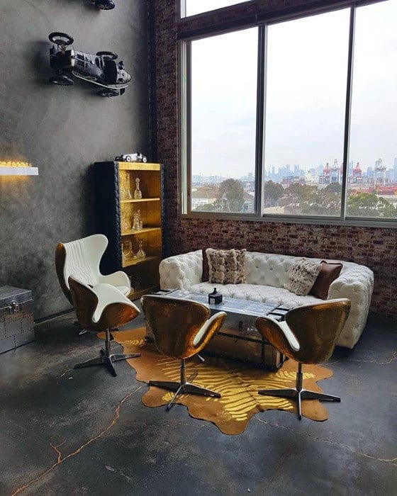 White tufted leather sofa with vintage chairs in an industrial loft with large windows.