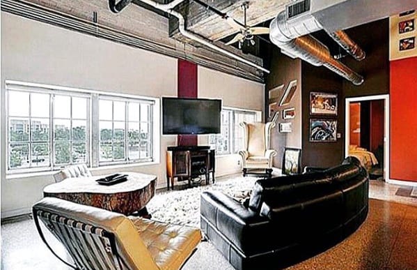 Black leather sectional sofa in an industrial loft with exposed ductwork and large windows.