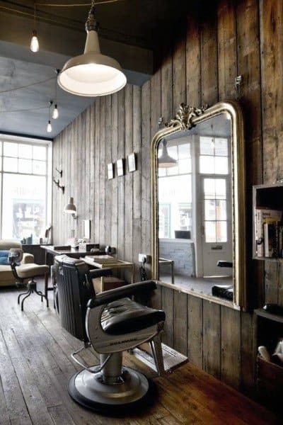 Rustic barbershop with wooden plank walls, ornate mirror, and vintage barber chair.