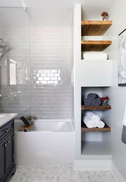 Small bathroom with light gray subway tile shower wall, built-in wooden shelves, and bathtub.