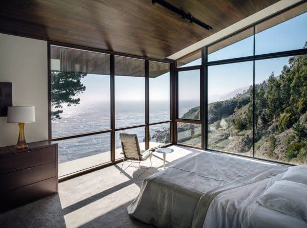 Bedroom with floor-to-ceiling glass windows, ocean and cliffside views, and modern decor.